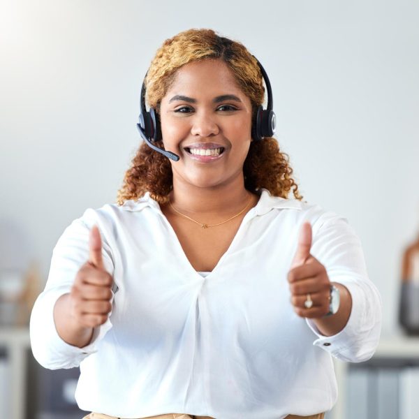 Thumbs up, crm and contact use with a call center agent working in customer service or telemarketing. Thank you, sales and support with a happy business woman working in her office with a headset.
